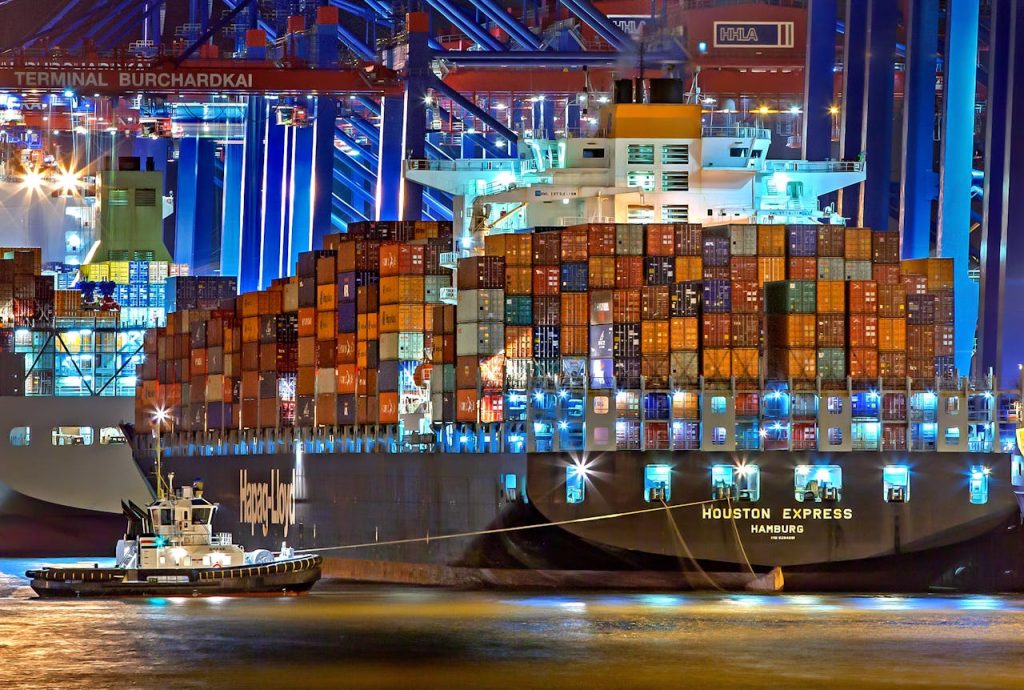 pexels photo 753331 A brightly lit cargo ship at Hamburg harbor with stacked containers and a tugboat.